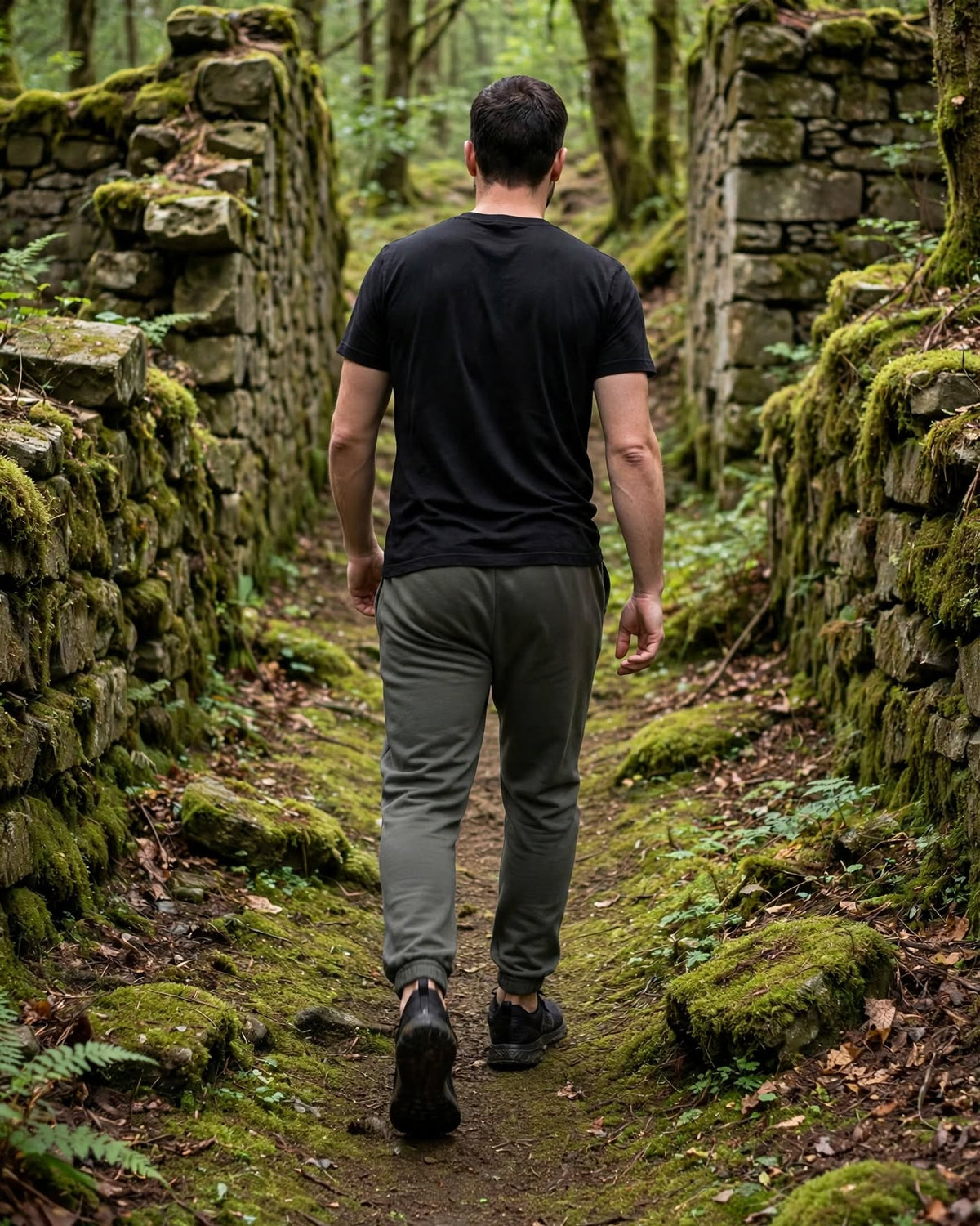 Back view of a man walking between ruined stone walls in plain-back Pepper REBILT joggers with elastic cuffs