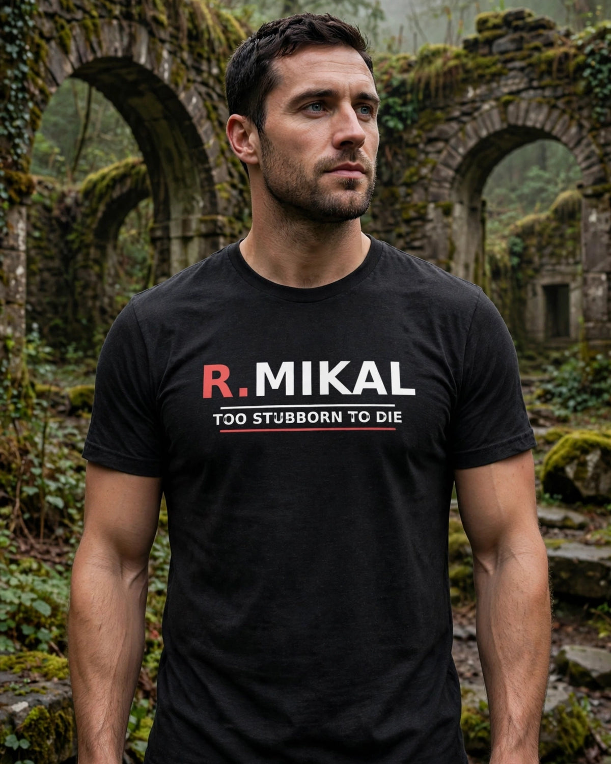 Man wearing the black heather R.Mikal Too Stubborn to Die tee in misty forest ruins, red R. and white MIKAL with TOO STUBBORN TO DIE between white and red lines
