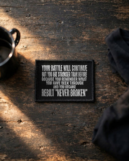Black REBILT Your Battle Will Continue embroidered patch on a weathered wooden table in morning light