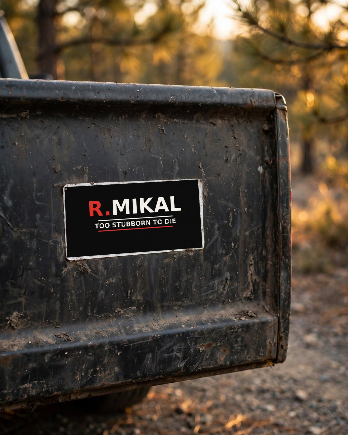 Black R.Mikal Too Stubborn to Die bumper sticker on the dusty tailgate of an old pickup truck